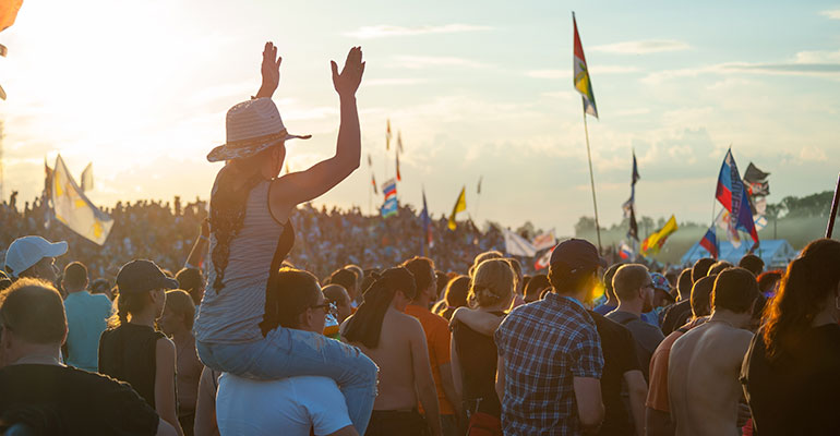 Coachella Festival- Woman on man’s shoulders, flags in the air, sunset over a festival