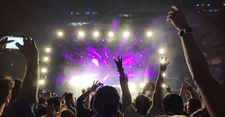 Sunburn Music Festival- View from the crowd at a festival, purple lights shine and hands wave in the air