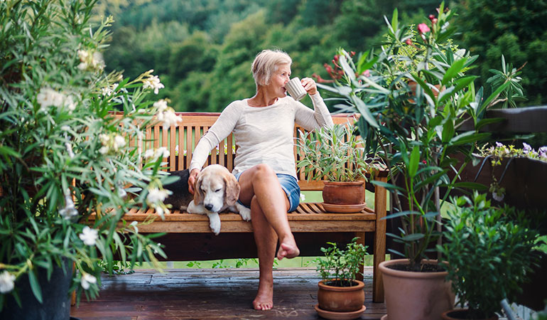 Retired woman drinking coffee on a bench with her dog