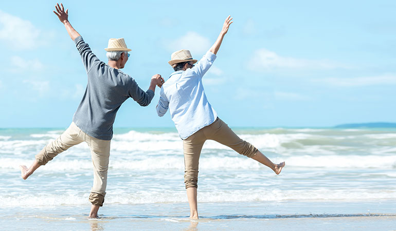 Retired couple paddling in the sea, legs and arms in the air, holding hands
