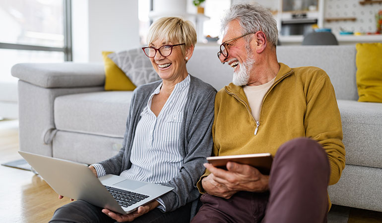 Retired couple sat on floor using laptop and iPad working out finances