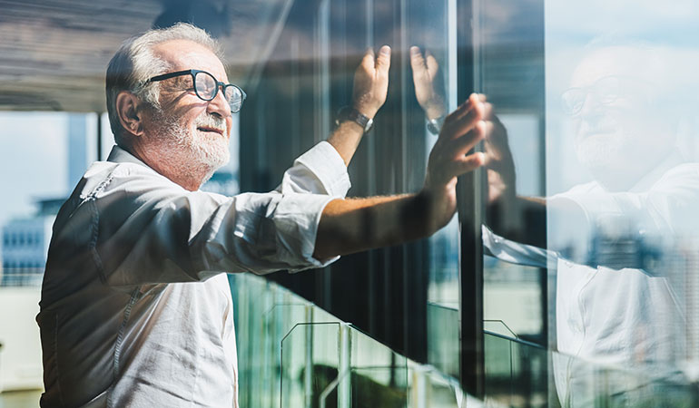 Retired man with hands on windows looking out into the distance